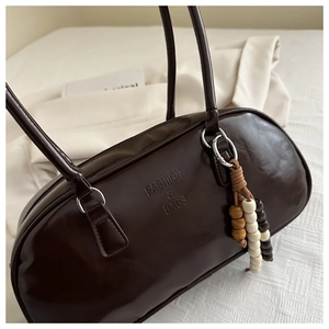 Detail of glossy chocolate leather shoulder bag with embossed logo and bead tassel charm