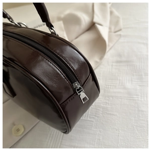 Detailed view of silver metal zipper and glossy dark brown patent leather on underarm bag