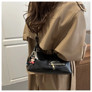 Detailed close-up of a glossy black shell bag with a metal zipper and cute calf charm