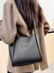 Classic black pebbled leather tote bag with gold lettering shown on a stylish model