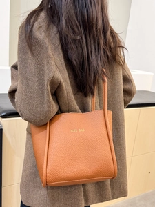 Brown textured leather tote bag with gold lettering shown from a stylish back view