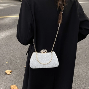 Elegant silver evening clutch bag with crystal crown clasp and gold chain over a black coat