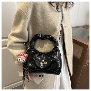 Close-up of black pleated faux leather handbag featuring a cute plush bear charm accessory