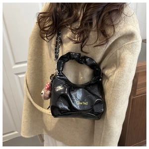 Detail of black pleated glossy handbag with chain strap and cute bear charm accessory