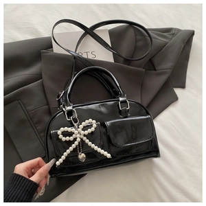 Detail of black patent leather Boston bag featuring pearl bow and silver heart pendant