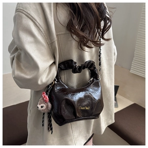 Detail view of brown pleated crossbody bag with chain strap and cute plush doll charm