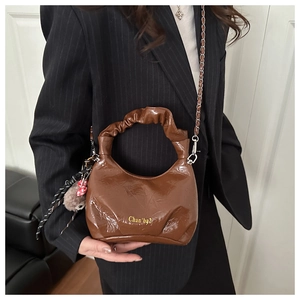 Detail of brown pleated handbag showing glossy leather texture and silver chain strap