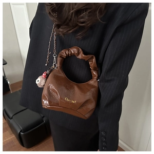 Detail of a brown pleated handle handbag with a gold logo and a cute bear charm pendant