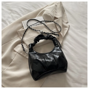 Close-up of black glossy pleated handbag with silver chain strap on beige blazer