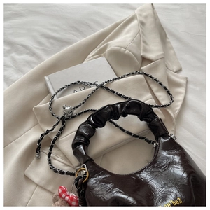 Detail of dark brown glossy wrinkled leather handbag with metallic chain and bow charm
