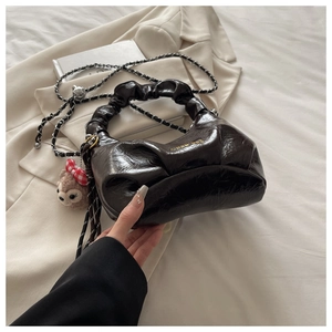 Detail of glossy black pleated handbag with silver chain and cute plush keychain