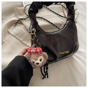 Detail of black pleated patent leather bag with silver chain and cute plush bear charm