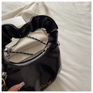Detailed close-up of a black pleated chain bag with glossy texture and golden logo