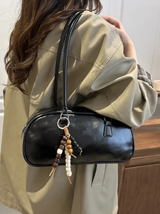 Minimalist black shiny leather underarm bag with wooden beads on khaki trench coat