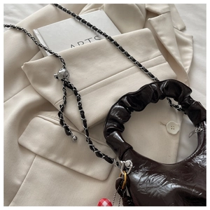 Detailed shot of dark brown ruched cloud bag with adjustable silver chain and red charm