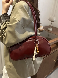 Fashionable burgundy underarm bag with beaded charm and glossy finish shown on model