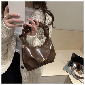 Detail of soft dark brown pleated handbag with a sleek glossy finish and golden logo