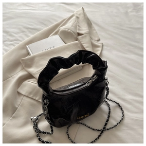 Detail of black glossy patent leather handbag with scrunchie handle and gold logo