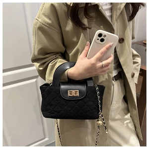 Detail of black quilted crossbody bag with gold twist-lock and chain strap on khaki coat