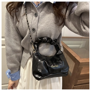 Detail of black glossy leather handbag featuring ruched handle and gold chain strap