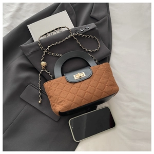Detail of brown quilted crossbody bag with golden lock and chain strap next to a phone