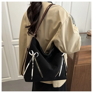 Détail du sac Hobo en toile noire avec fermetures éclair et ruban décoratif sur la bandoulière