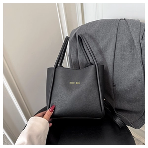 Detail der schwarzen Tote Bag mit Lychee-Struktur und gelbem Logo auf grauem Blazer
