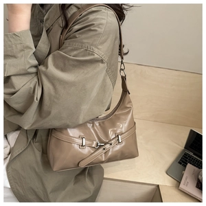 Detail of khaki patent leather crescent shoulder bag featuring silver buckle and zip closure