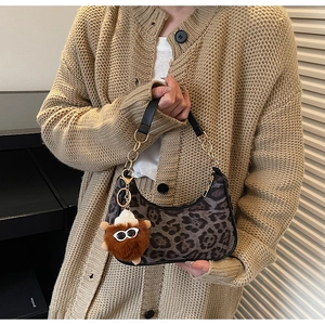 Détail du sac hobo léopard avec breloque en peluche et chaîne dorée porté par un modèle