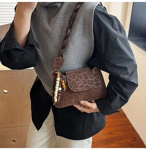 Detail of leopard print handbag featuring a unique braided handle and wooden bead tassel