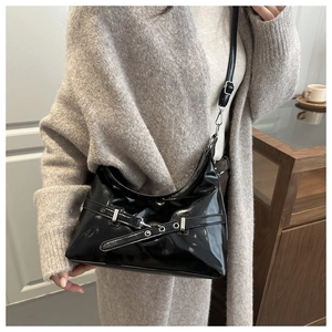 Detail shot of black patent leather hobo bag featuring silver hardware and eyelet belt straps