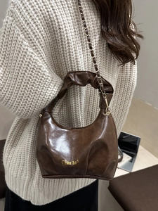 Brown pleated faux leather shoulder bag with gold chain strap shown on model shoulder