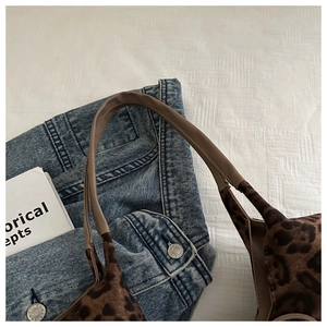 Flat lay detail of leopard print tote bag with brown leather handle on denim fabric