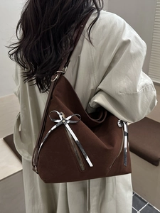 Grand sac à bandoulière marron foncé avec nœud argenté porté par un mannequin