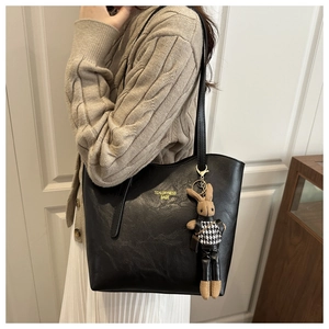 Detail of black faux leather tote bag with printed text and cute bunny plush charm