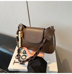 Close-up of brown matte leather bag featuring a woven strap and beaded pendant detail
