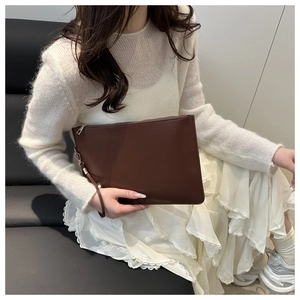 Detail of dark brown clutch bag with golden zipper and detachable wrist strap
