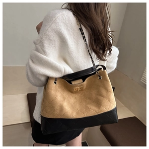 Detail of quilted bucket bag with chain strap and gold twist-lock on a camel suede surface