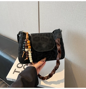 Detail of black leopard print crossbody bag with woven handle and beaded tassel charm