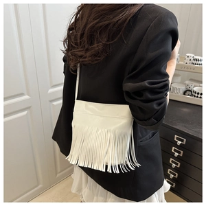 Detailed view of a white faux leather shoulder bag featuring long decorative tassels
