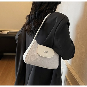 Side view of white crocodile pattern shoulder bag with silver bow buckle on model