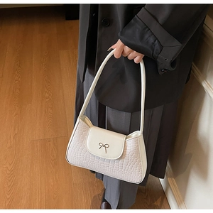Detail view of cream white crocodile texture handbag with gold bow buckle on a model