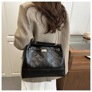 Detail of classic black quilted tote bag with gold lock and chain strap on shoulder