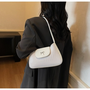 Detail of white crocodile pattern shoulder bag featuring a metal bow and retro texture
