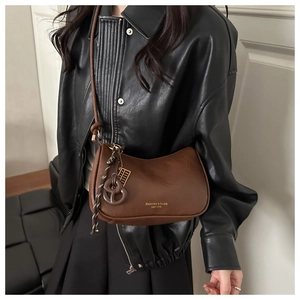 Detail of a brown leather shoulder bag with gold lettering and a unique rope pendant charm