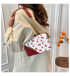 Crossbody bag with red and white cherry print, gold chain strap, shown on a model