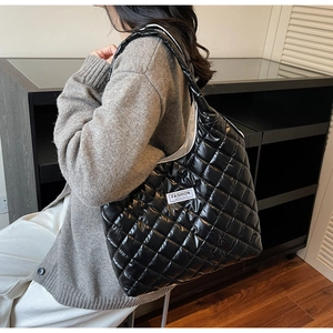 Macro detail of black quilted puffer tote bag with glossy finish and logo patch