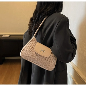 Detail of a beige crocodile-embossed half-moon underarm bag with a silver bow accent