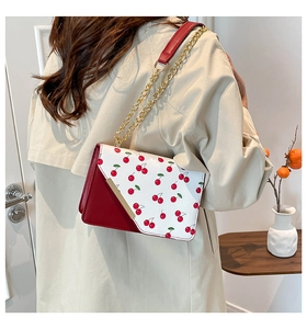 Detail of red cherry print on shoulder bag with gold chain and metal trim accents
