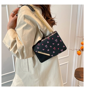 Detail of black crossbody bag with pink bow prints and gold chain strap on model